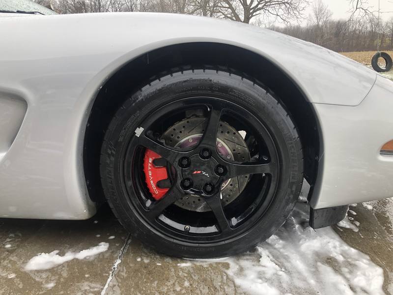 Mobile exterior detailing in Charlotte: Close-up of a silver Corvette's glossy black wheel, red brake caliper, and shined tire after a wash